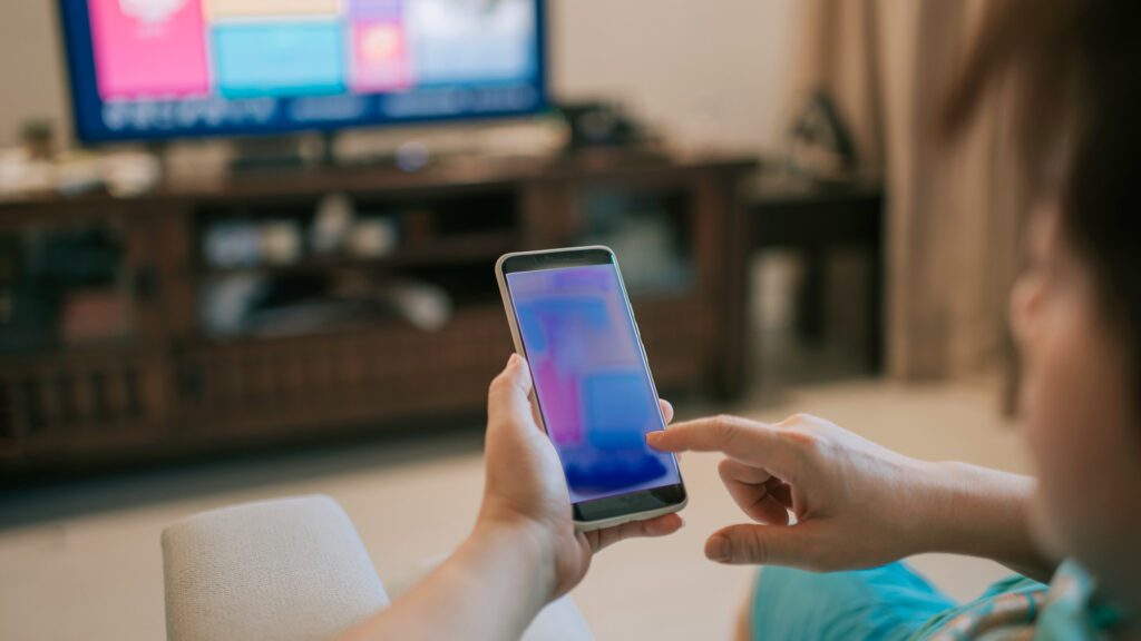 A person scrolls on their phone while watching TV